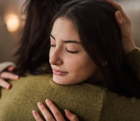 Young teenage girl hugging her mother at home.